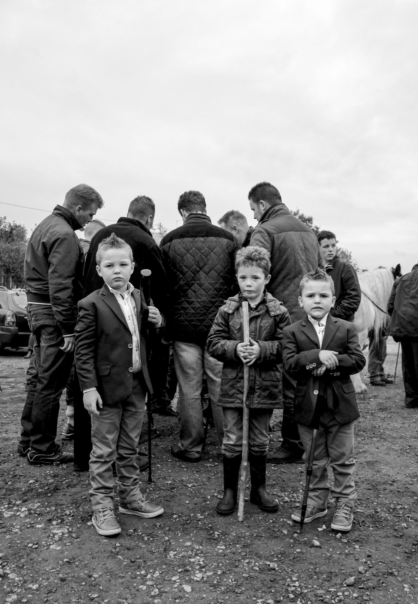 Drei Jungen mit Stöcken stehen vor einer Gruppe Männer