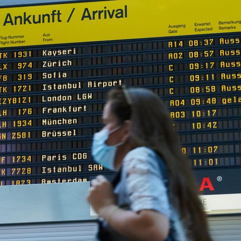 Berlin: Vor der Ankunfts-Anzeigetafel geht eine Reisende mit Mundschutz durch den Flughafen Tegel