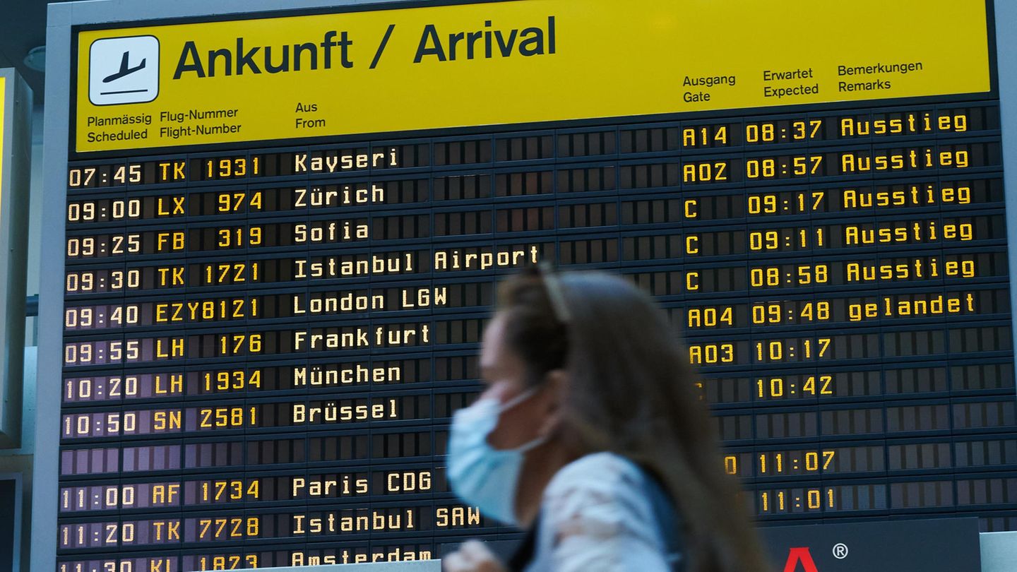 Berlin: Vor der Ankunfts-Anzeigetafel geht eine Reisende mit Mundschutz durch den Flughafen Tegel
