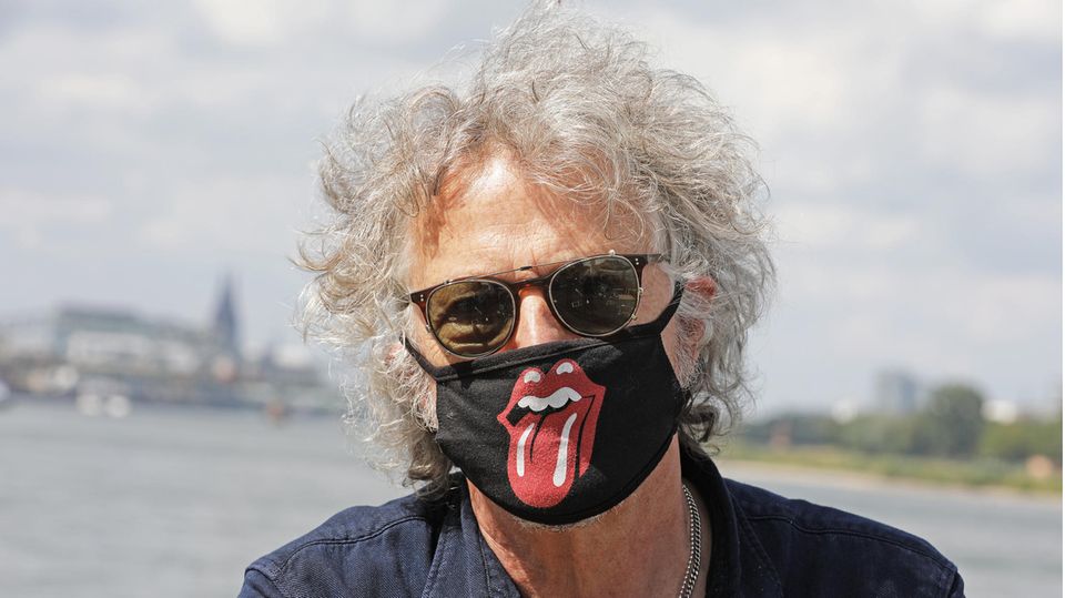 Ein Mann mit grauer Lockenmähne trägt eine Sonnenbrille und einen Mund-Nase-Schutz mit dem Logo der "Rolling Stones"