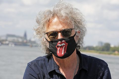 Ein Mann mit grauer Lockenmähne trägt eine Sonnenbrille und einen Mund-Nase-Schutz mit dem Logo der "Rolling Stones"