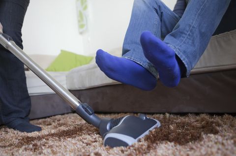 Ein Mann hebt seine Beine, während eine Frau den Teppich saugt