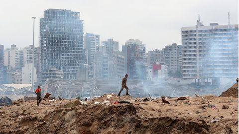 Ein Soldat geht über den Ort einer Explosion im Hafen, während im Hintergrund schwer beschädigte Gebäude zu sehen sind