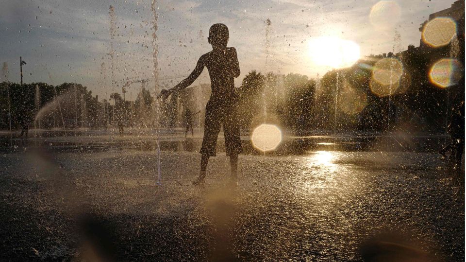 Kind kühlt sich bei großer Hitze in einem Springbrunnen ab