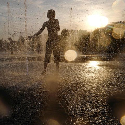 Kind kühlt sich bei großer Hitze in einem Springbrunnen ab