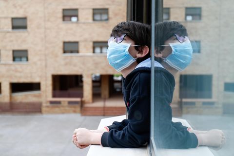 Ein Kind mit Mundschutz schaut aus dem Fenster seines Hauses