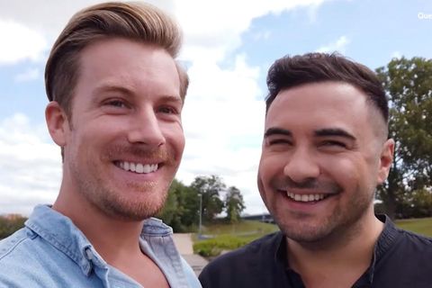Links lächelt ein größerer blonder Mann in die Kamera, rechts ein etwas kleinerer dunkelhaariger Mann. Beide tragen Scheitel