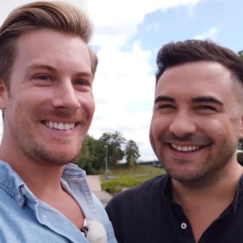 Links lächelt ein größerer blonder Mann in die Kamera, rechts ein etwas kleinerer dunkelhaariger Mann. Beide tragen Scheitel