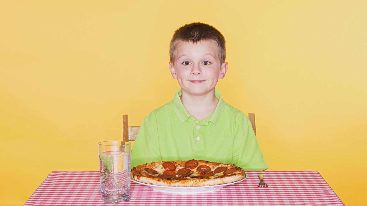 Ein Junge sitzt vor einer Pizza
