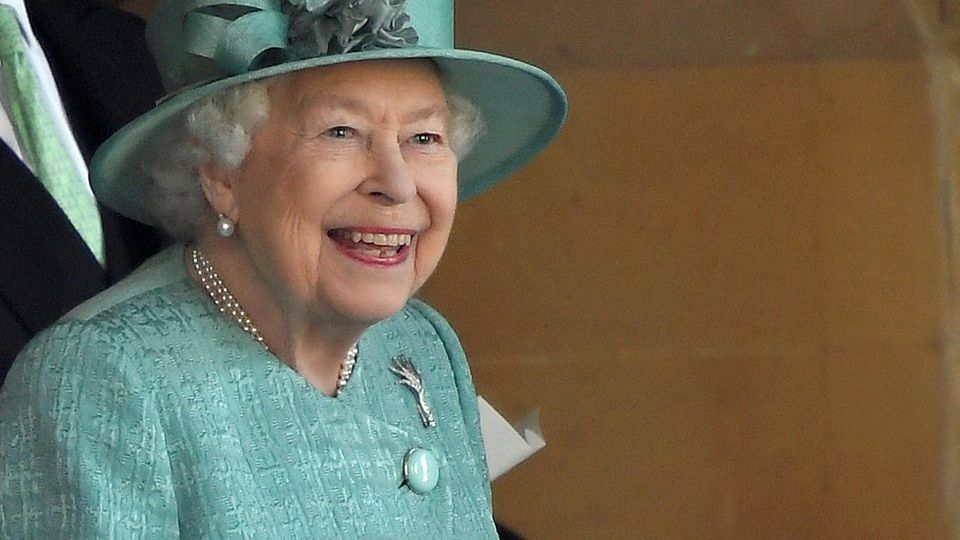 Queen Elizabeth steht in mintgrünem Kostüm und passendem Hut auf einer Tribüne und lächelt breit