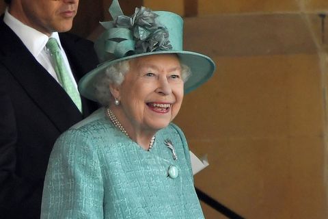 Queen Elizabeth steht in mintgrünem Kostüm und passendem Hut auf einer Tribüne und lächelt breit