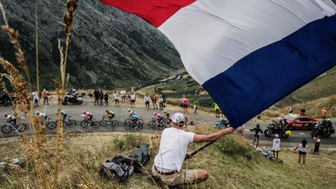 Tour de France 2020: Radsportfan schwenkt Frankreich-Fahne an einem Berg, unterhalb das Fahrerfeld