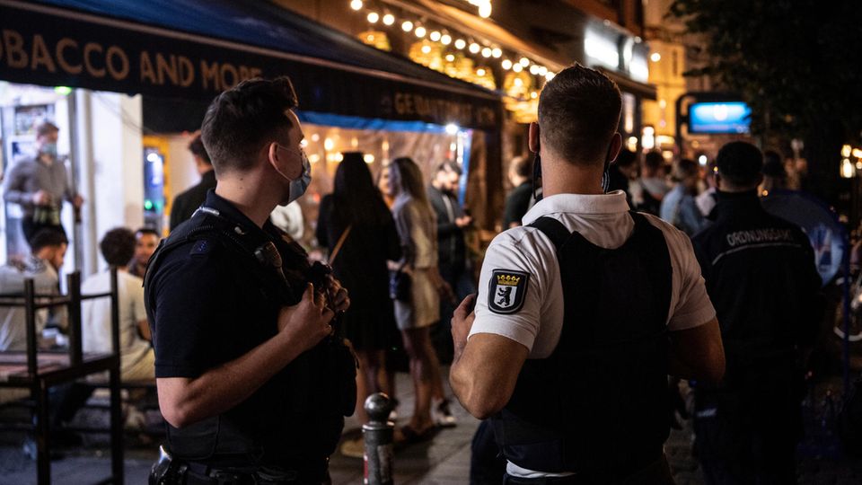 Ein Polizeibeamter und ein Mitarbeiter des Ordnungsamtes stehen vor einem Lokal in Berlin