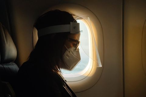 Eine Frau sitzt mit Mund-Nasen-Schutz in einem Flugzeug