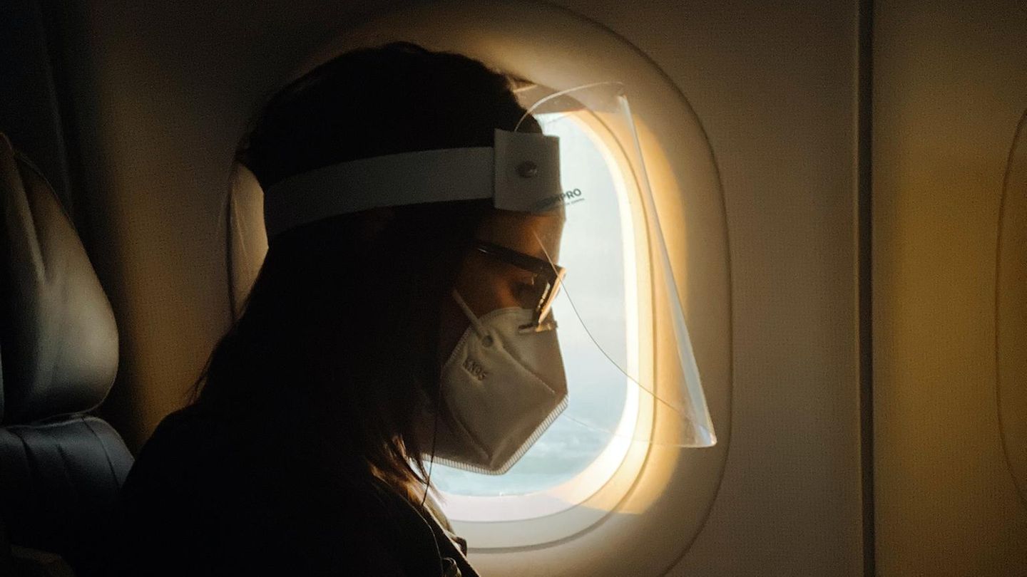 Eine Frau sitzt mit Mund-Nasen-Schutz in einem Flugzeug