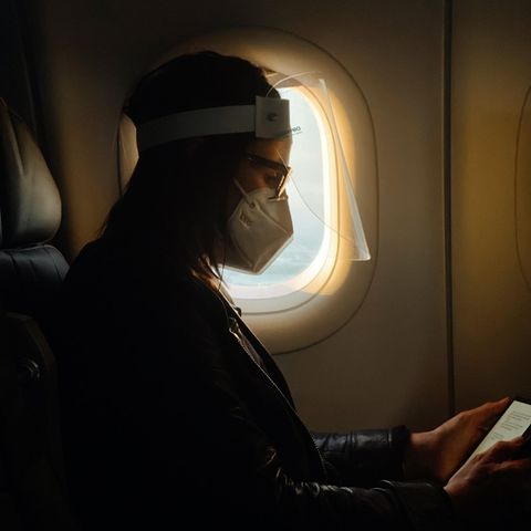 Eine Frau sitzt mit Mund-Nasen-Schutz in einem Flugzeug