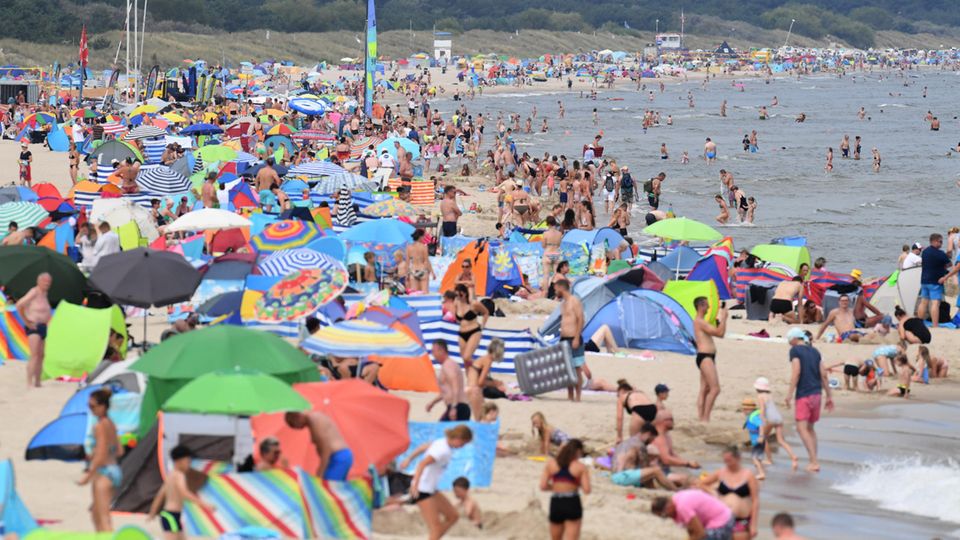 Am Ostseestrand vor der Seebrücke haben sich zahlreiche Badegäste am Strand niedergelassen