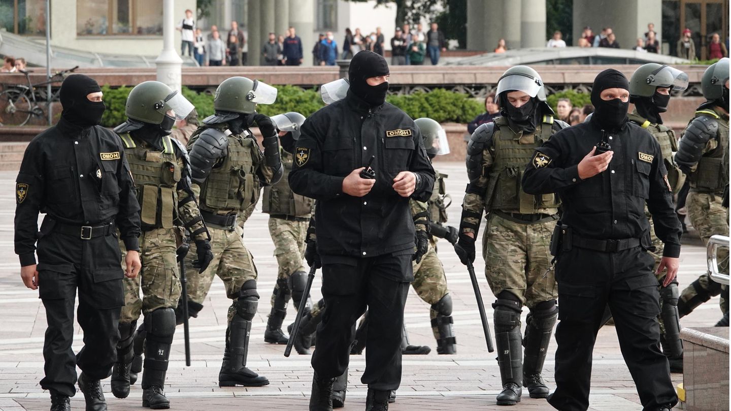 Polizisten in grüner oder schwarzer Kampfmontur - manche mit Sturmhauben - gehen in einer ungeordneten Gruppe über einen Platz