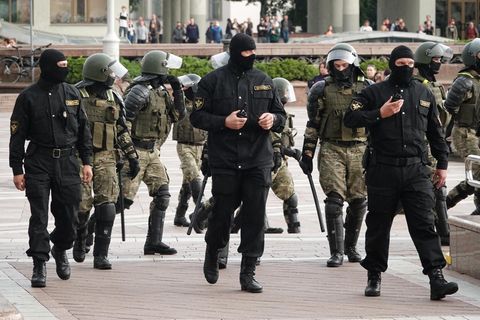 Polizisten in grüner oder schwarzer Kampfmontur - manche mit Sturmhauben - gehen in einer ungeordneten Gruppe über einen Platz