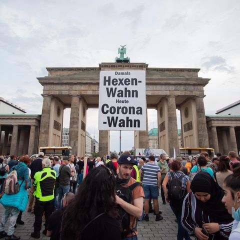 Vor dem Brandenburger Tor in Berlin steht eine Menschenmenge. Jemand hält ein Schild "Damals Hexenwahn, heute Coronawahn" hoch