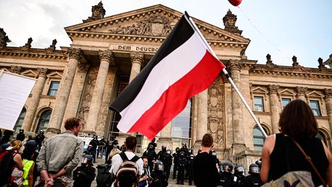Teilnehmer der Berliner Kundgebung gegen die Corona-Maßnahmen stehen vor dem Reichstag, ein Teilnehmer hält eine Reichsflagge mit schwarz-weiß-roten Querstreifen.