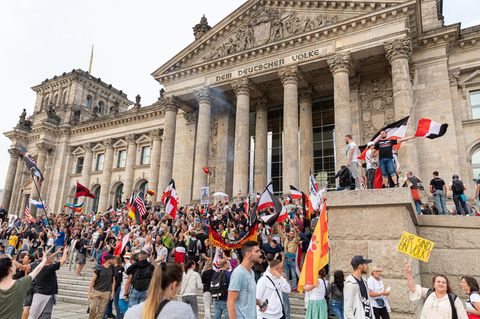 Demonstranten mit Reichsflaggen stehen auf den Stufen vor dem Reichstag in Berlin