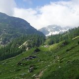 Rückblick: Der Pfad leitet zur unscheinbaren Alpe Sfille mit dem schneebedeckten Hängen des Pizzo dell'Alpe Gelato im Hintergrund.