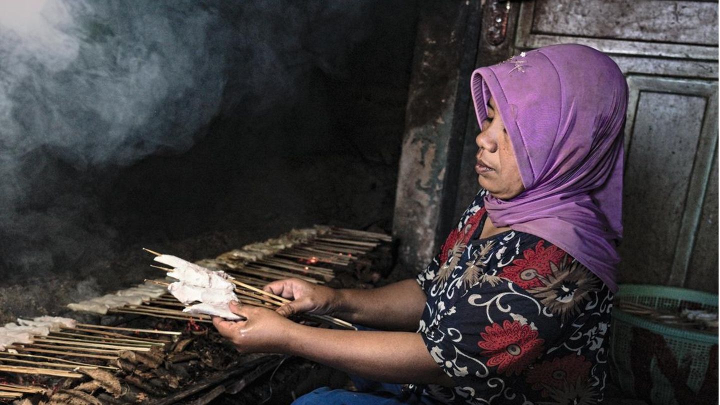 Indonesia, Lombok island, July 2019. A woman working inside a shark warehouse is cooking skewers made with shark meat. In contrast with the high value of the fins, the meat is worth less than most fish and is often consumed locally by lower classes. Eine Frau grillt das Fleisch eines Haifischs