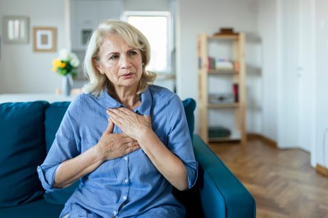 Eine ältere Frau hält sich die Brust