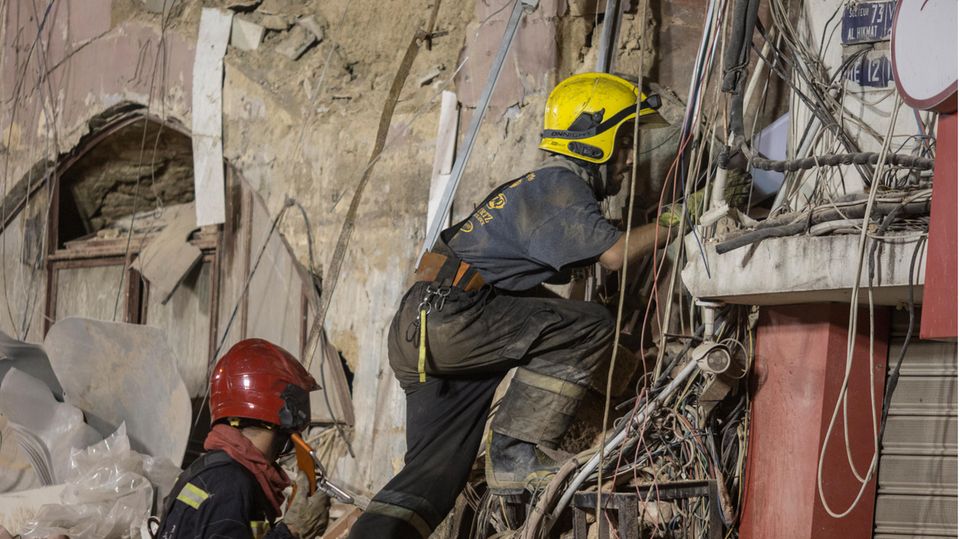 Zwei Retter - einer mit rotem, einer mit gelbem Helm - klettern in den Trümmern eines eingestürzten Gebäudes