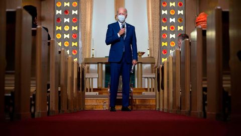 Ein weißhaariger Mann mit Atemmaske und blauem Anzug spricht im Mittelgang einer Kirche in ein Mikro