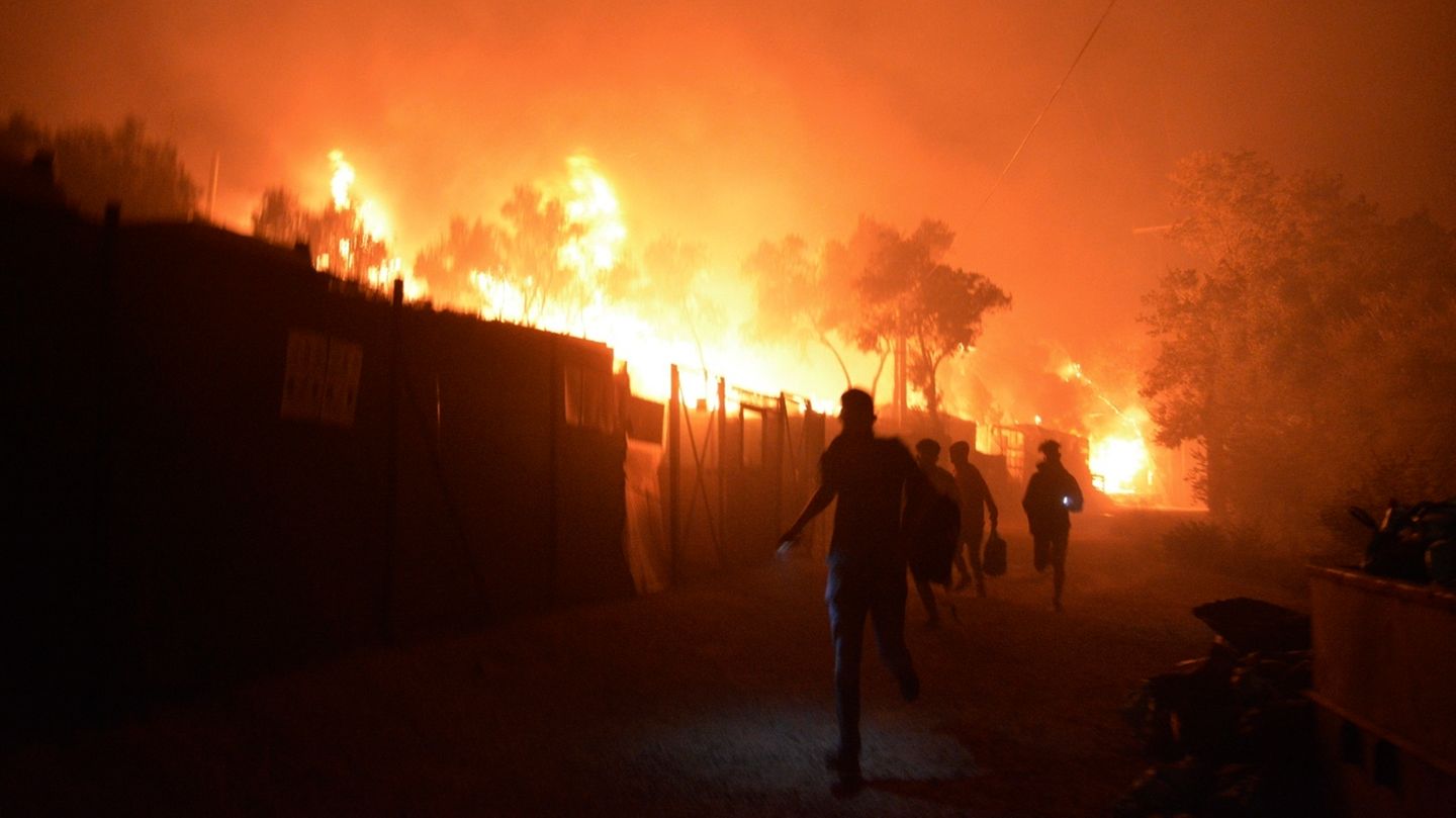Migranten rennen während ein Feuer im Flüchtlingslager Moria auf der Insel Lesbos brennt. Medienberichten zufolge stehen auch Wohncontainer in Flammen, weshalb die Behörden das Lager evakuierten.