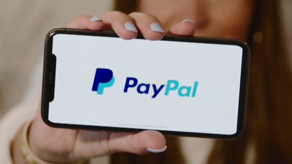 Eine Frau hält ihr Smartphone mit dem "PayPal"-Logo vor der Kamera.