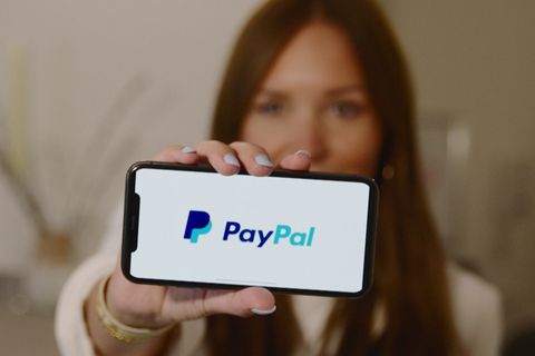 Eine Frau hält ihr Smartphone mit dem "PayPal"-Logo vor der Kamera.