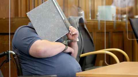Einer von zwei Angeklagten wird von Justizbeamten mit dem Rollstuhl in den Gerichtssaal gefahren