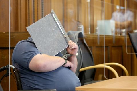 Einer von zwei Angeklagten wird von Justizbeamten mit dem Rollstuhl in den Gerichtssaal gefahren