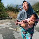 Frau hält ihr Baby auf der Flucht vor einem kleinen Feuer auf einem Feld in der Nähe der Stadt Mytilene