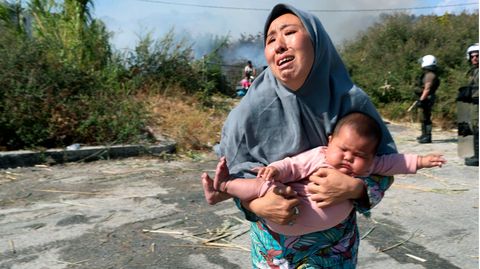 Frau hält ihr Baby auf der Flucht vor einem kleinen Feuer auf einem Feld in der Nähe der Stadt Mytilene