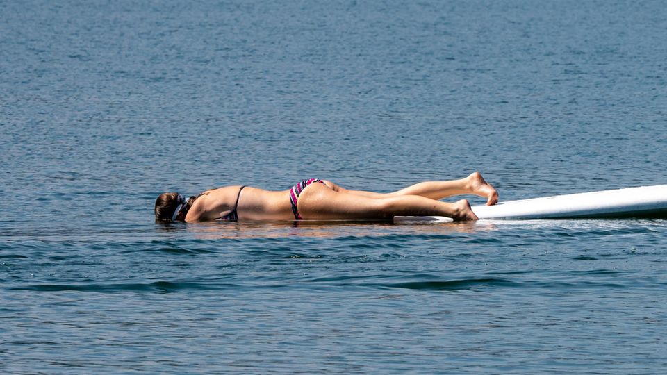 Flucht vor der Hitze: Eine junge Frau liegt im Riegsee auf einem Surfboard