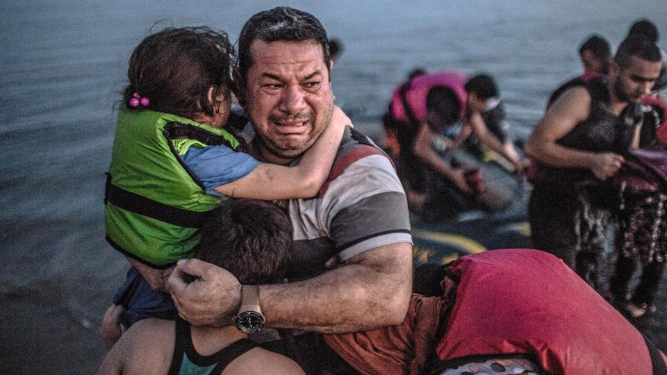 A Syrian refugee from Deir Ezzor, holding his son and daughter, breaks out in tears of joy after arriving via a flimsy inflatable boat crammed with about 15 men, women and children on the shore of the island of Kos in Greece, Aug. 15, 2015. The crossing... Laith Majid al-Amiri hält sein Kind im Arm