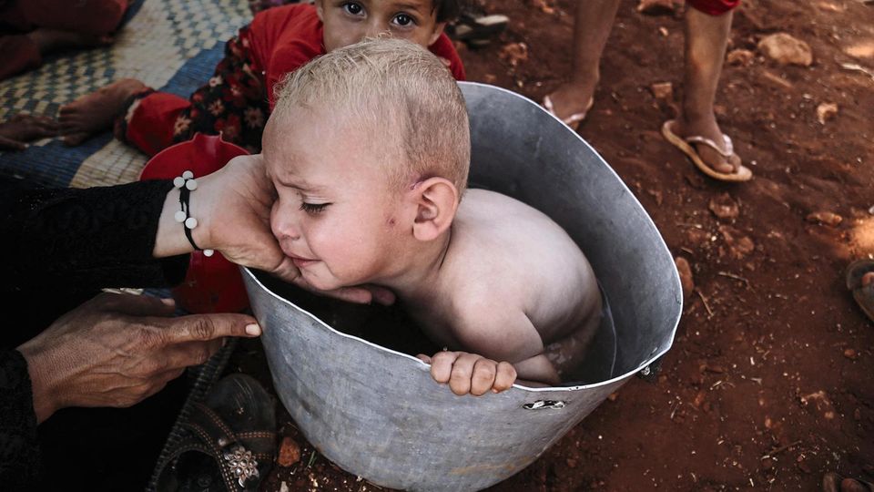 IDLIB, SYRIA - AUGUST 28: A Syrian baby bathing in a bucket outside a makeshift tent among olive trees on their way from Syria’s de-escalation zones in Idlib, Syria on August 28, 2019. Civilians, who have been displaced from the de-escalation zones in... Ein Baby wird in einem Eimer gebadet