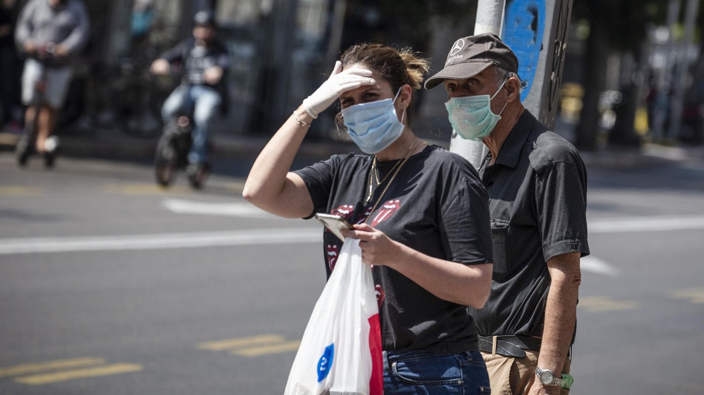 Israel, Tel Aviv: Passanten mit Mundschutz stehen auf der Straße