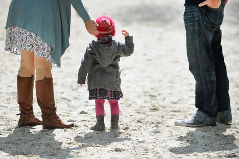 Ein Kind steht auf einem Spielplatz zwischen seinen Eltern