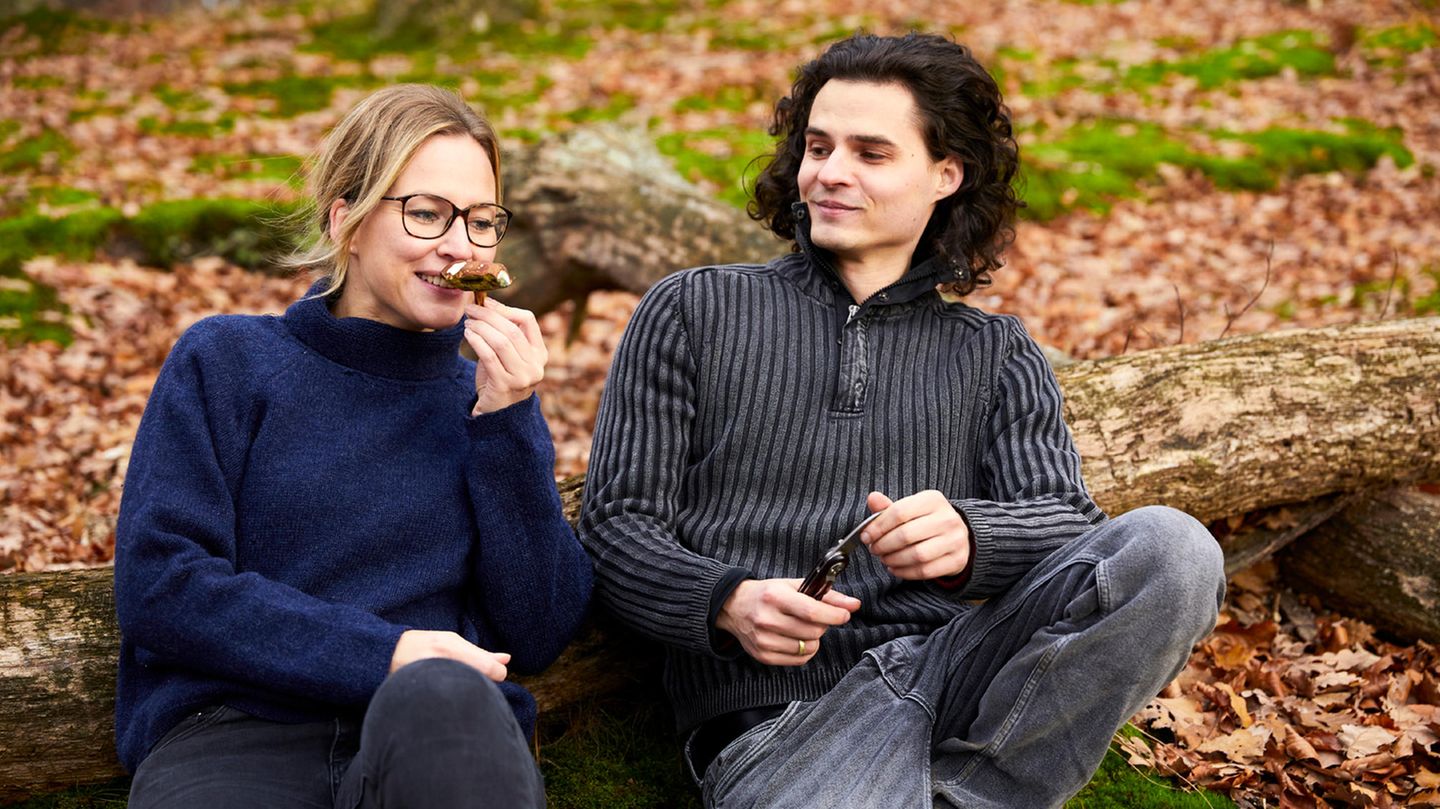Der Autor und eine Frau sitzen im Wald, sie riecht an einem Pilz
