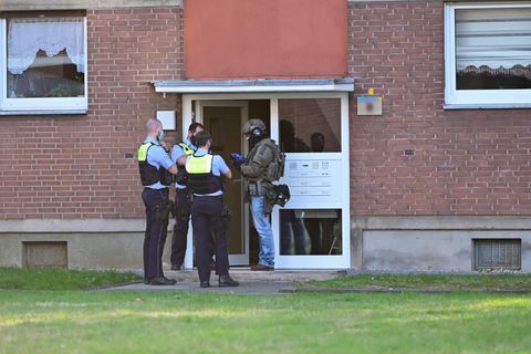 Polizei und ein SEK-Beamter stehen vor der Eingangstür eines Mehrfamilienhauses