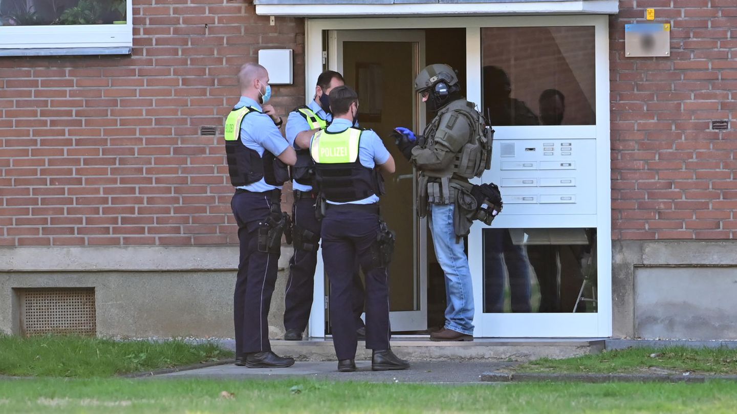Polizei und ein SEK-Beamter stehen vor der Eingangstür eines Mehrfamilienhauses