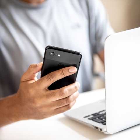Wlan Passwort anzeigen: Junger Mann sitzt mit Smartphone in der Hand vor einem Laptop