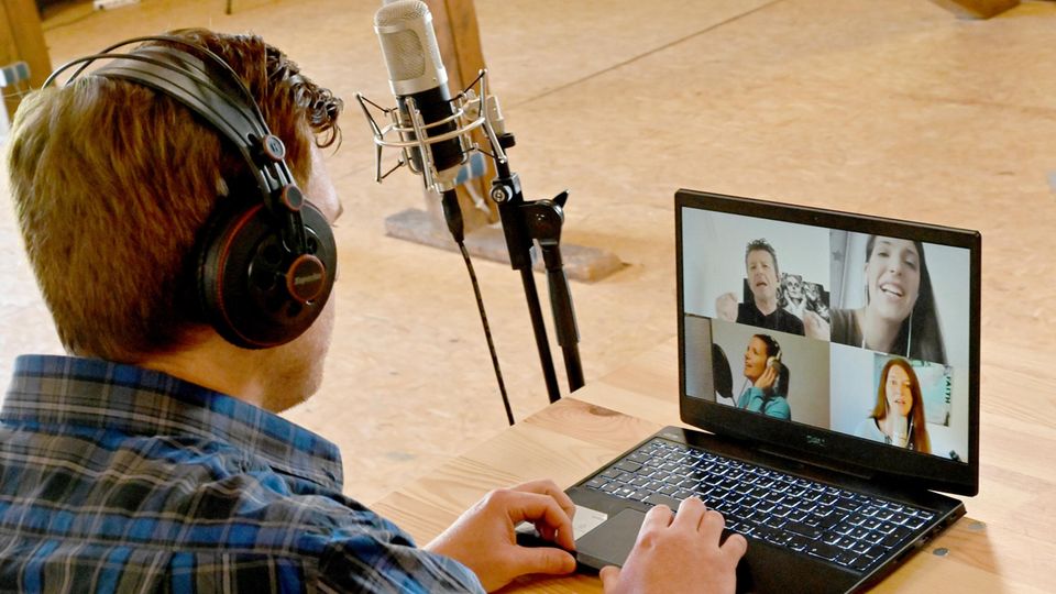 Ein Mann in blauem Karohemd sitzt an einem Laptop, auf dessen Monitor die Gesichter von vier Jugendlichen zu sehen sind