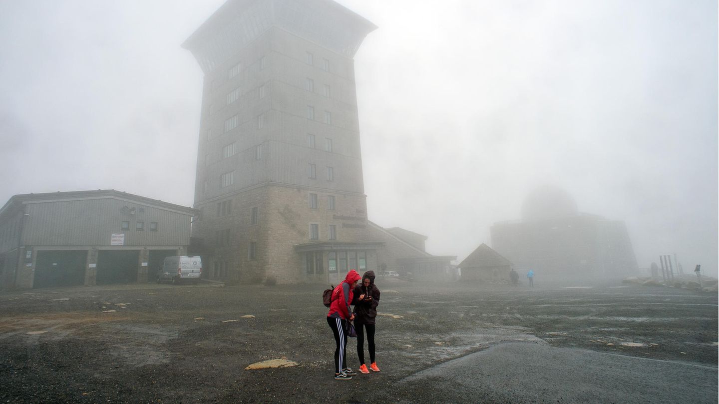 Zwei Touristinnen stehen mitten im Sturm auf dem Brocken vor dem Brokenhotel