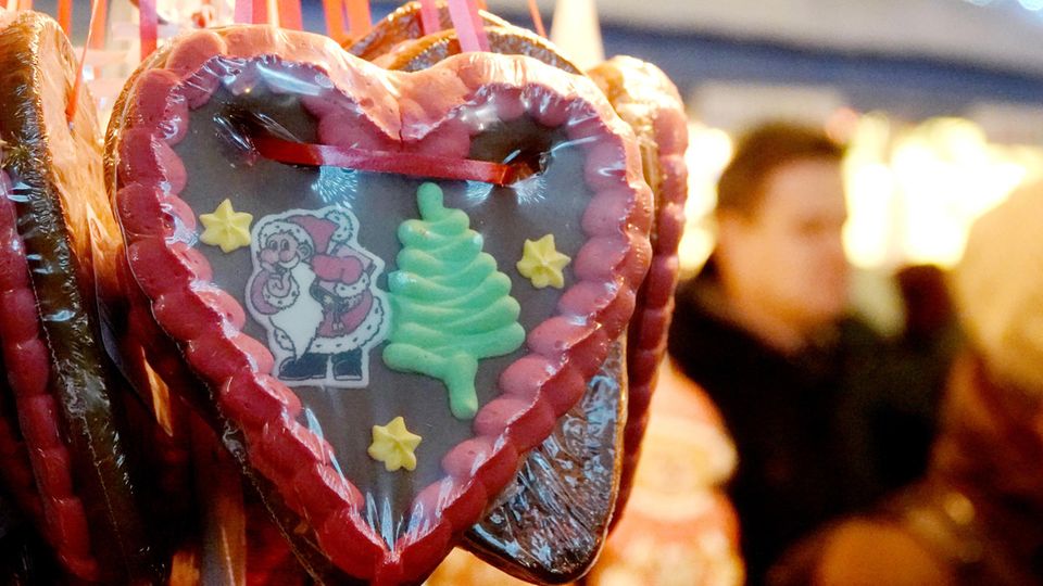 Ein Lebkuchenherz mit einem Tannenbaum und einem Weihnachstmann hängt an einem Stand auf einem Weihnachtsmarkt